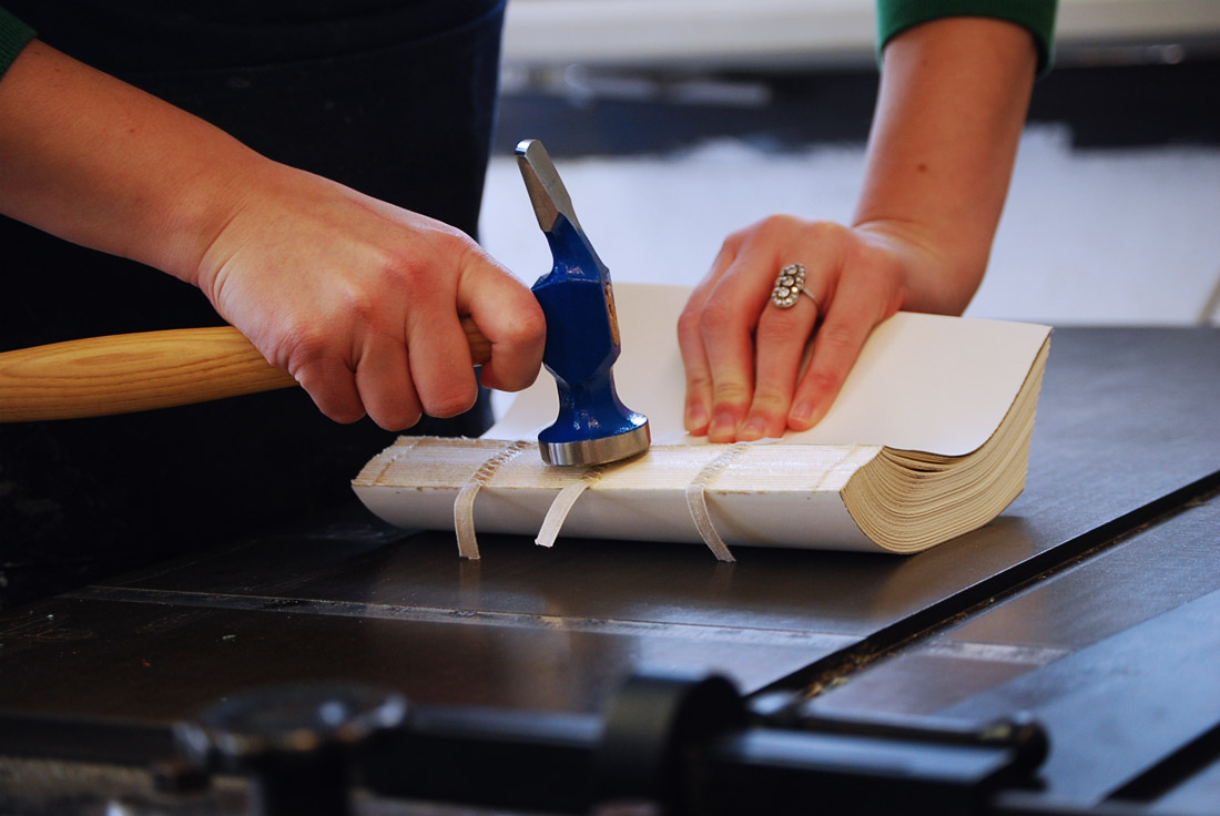 Artist hammering the spine of a binding.