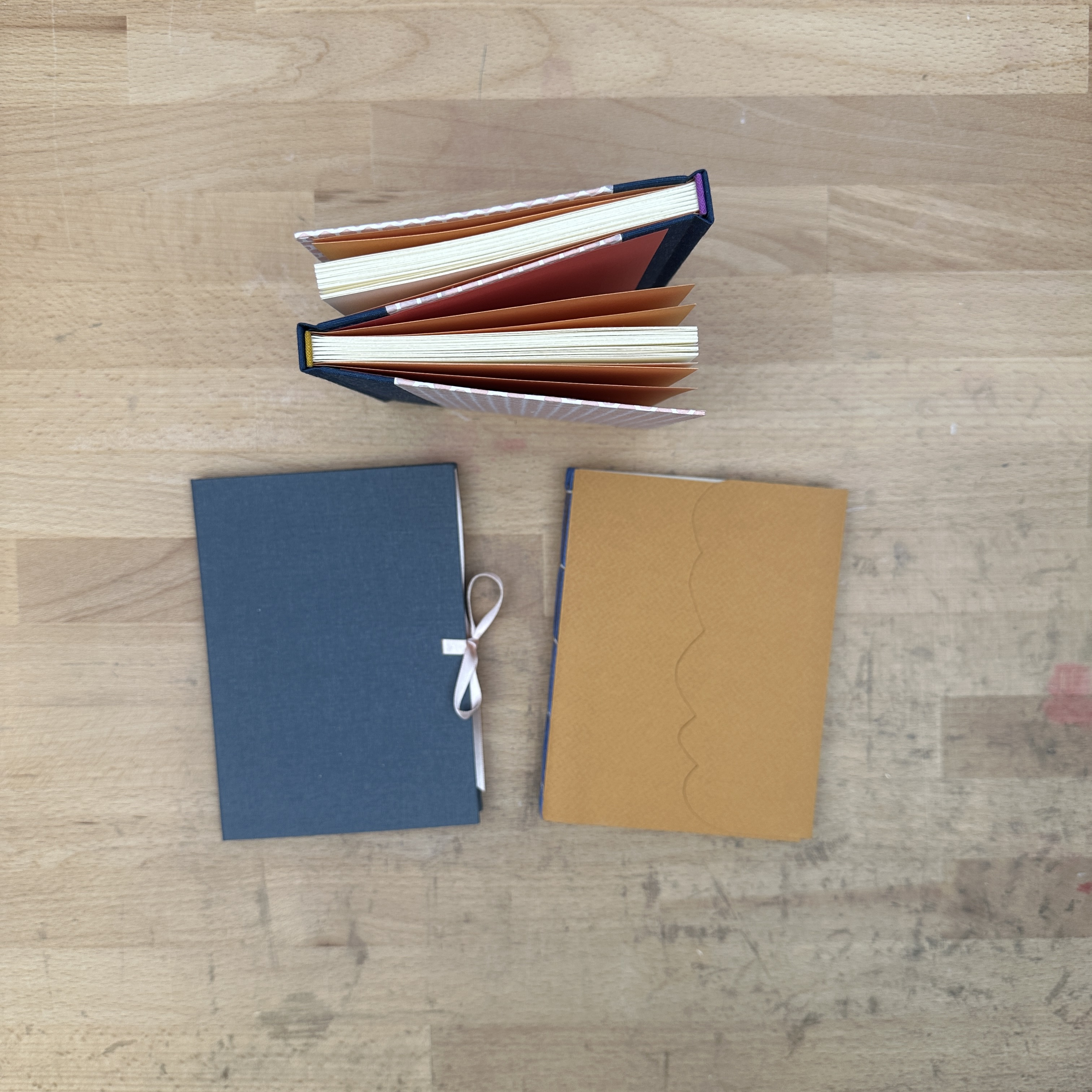 Two books laying flat on a wooden table and one book standing up.