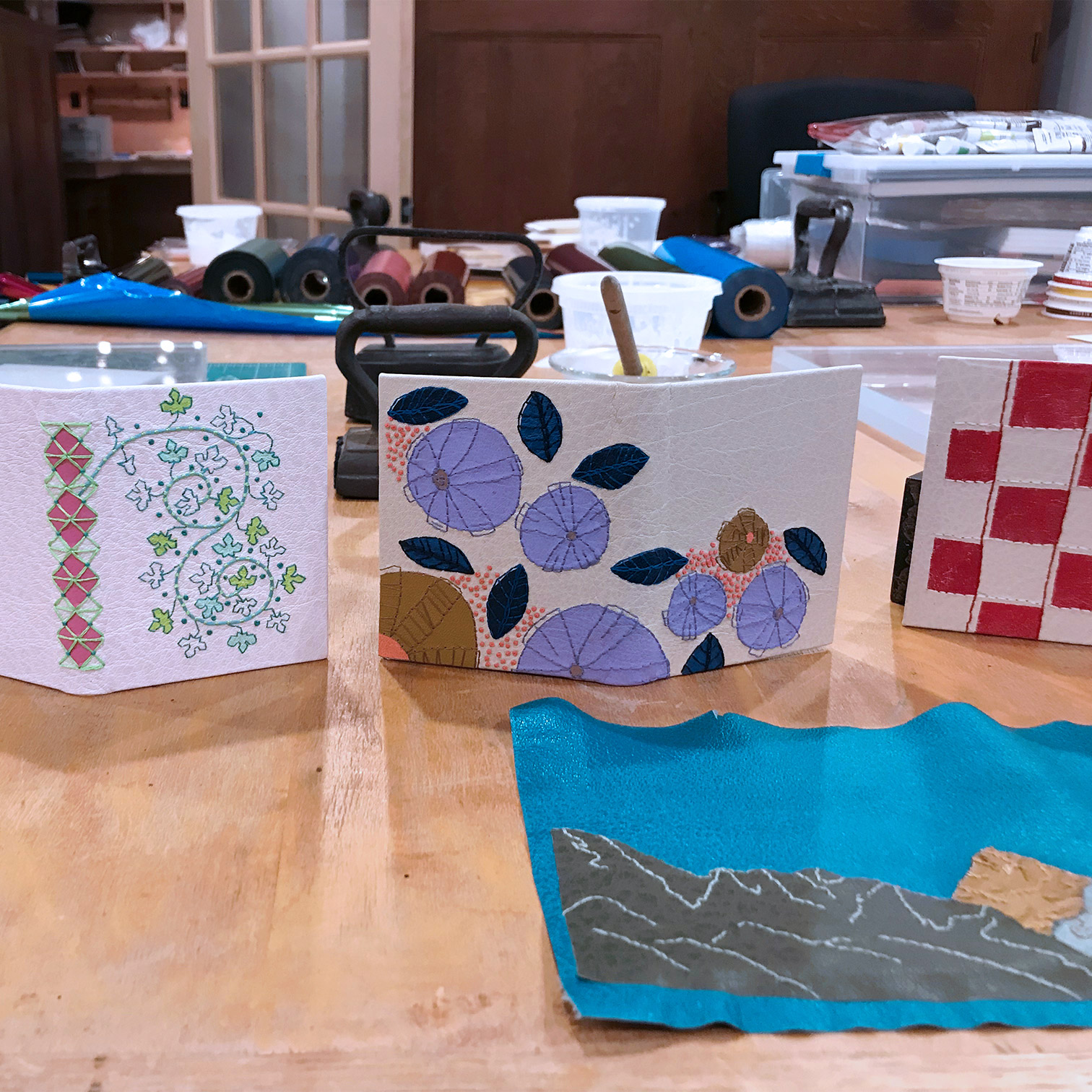 A variety of embroidered bindings on a wooden table.