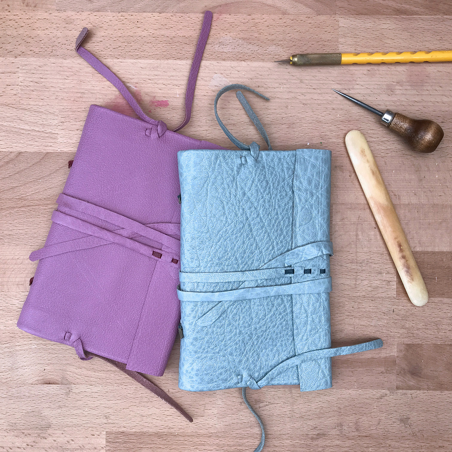 Two Modern Nag Hammadi bindings laying on a wooden table with some bookbinding tools.