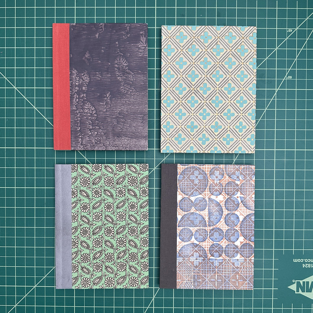 Four variations of sewn boards bindings sitting on a green cutting mat.