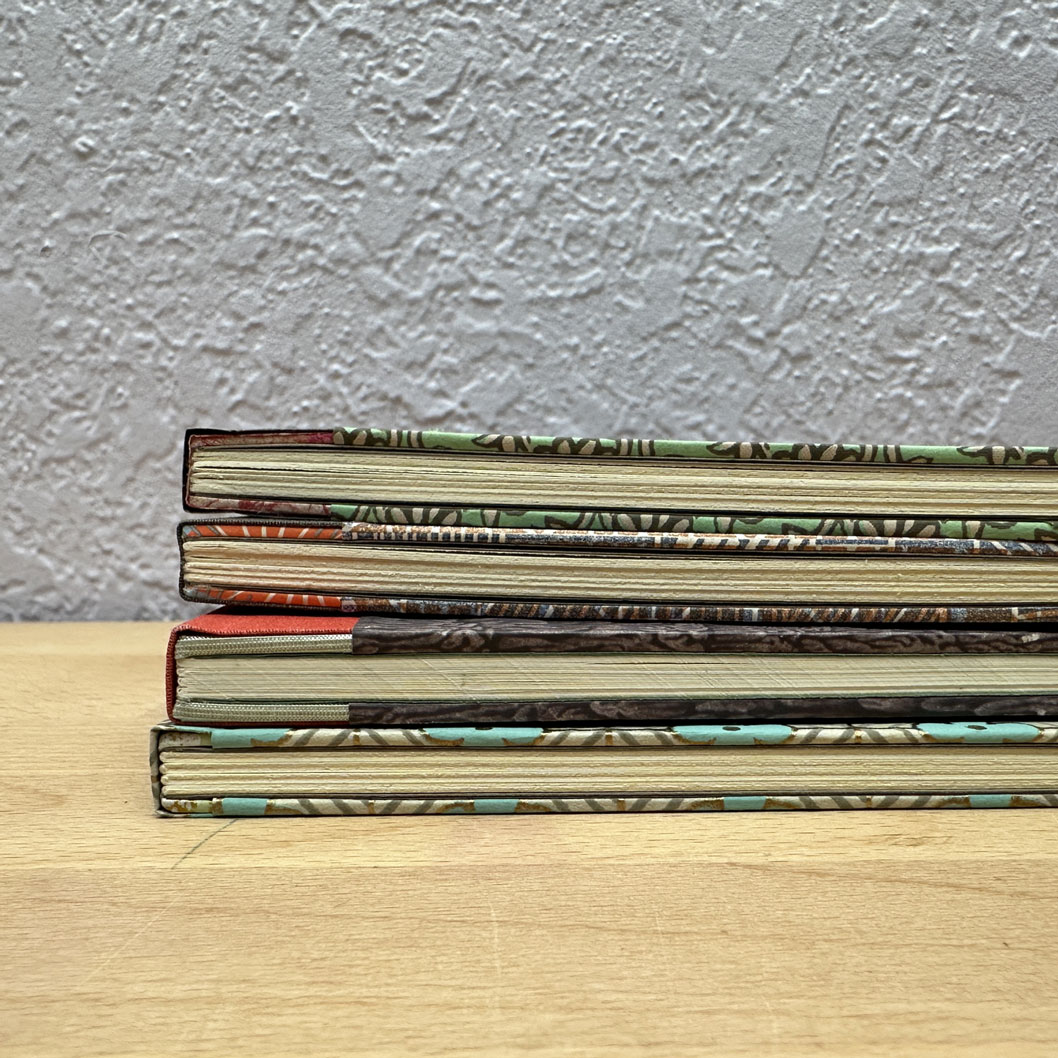 Stack of sewn boards bindings sitting on a wooden table.